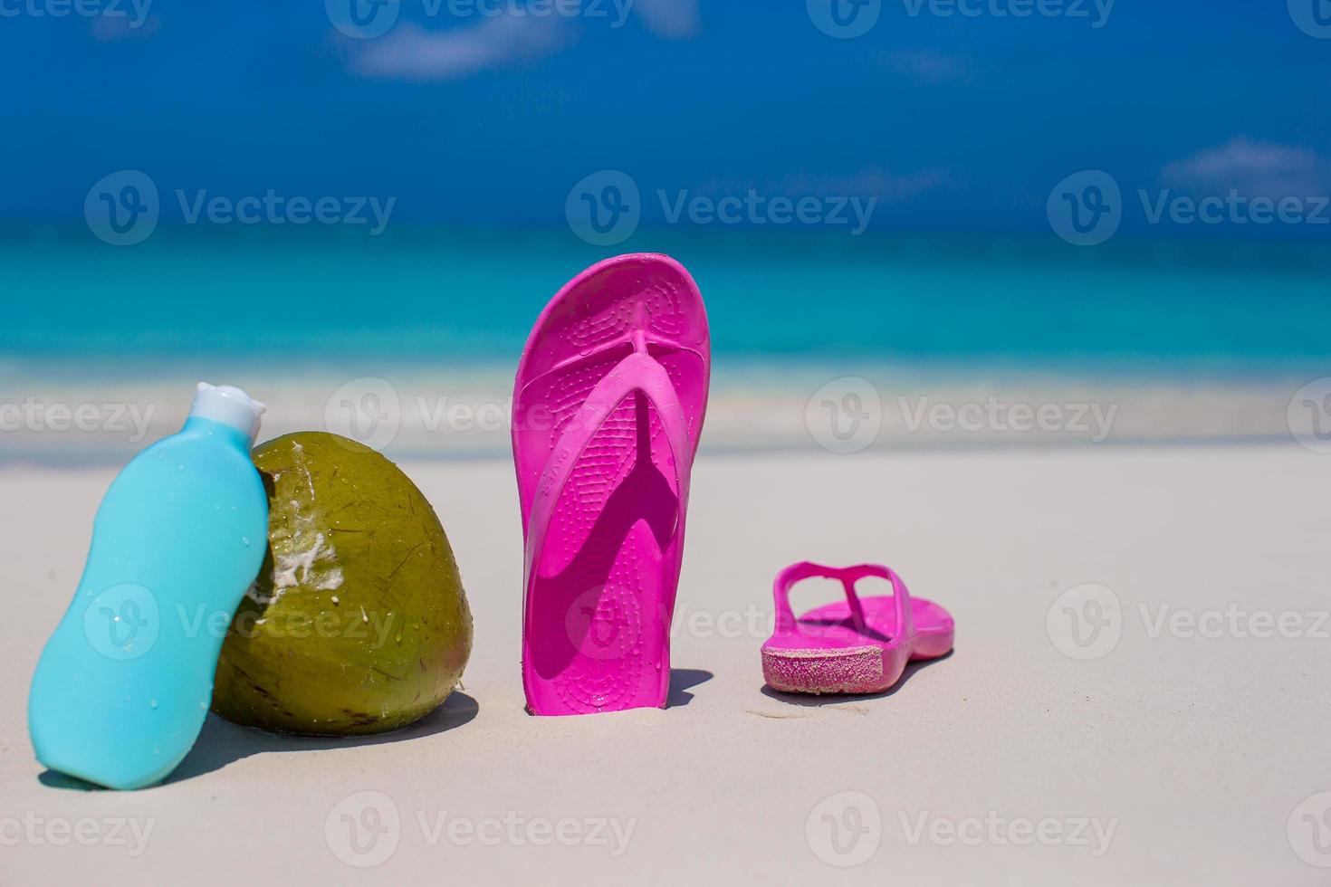Flip flops, coconut and suncream on white sand photo