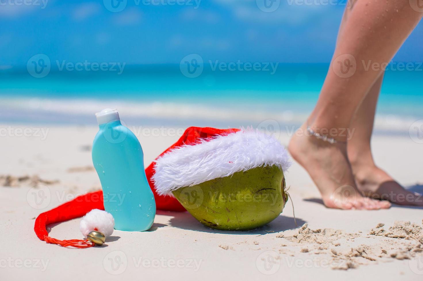 Suncream, Santa Hat on coconut and tanned female legs at white beach photo