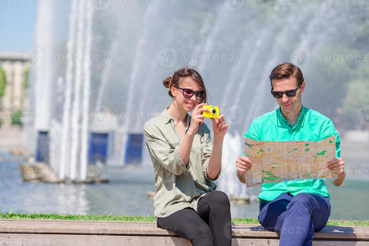Young tourist friends traveling on holidays in Europe smiling happy. Girl taking photos in the park and man with city map in search of attractions