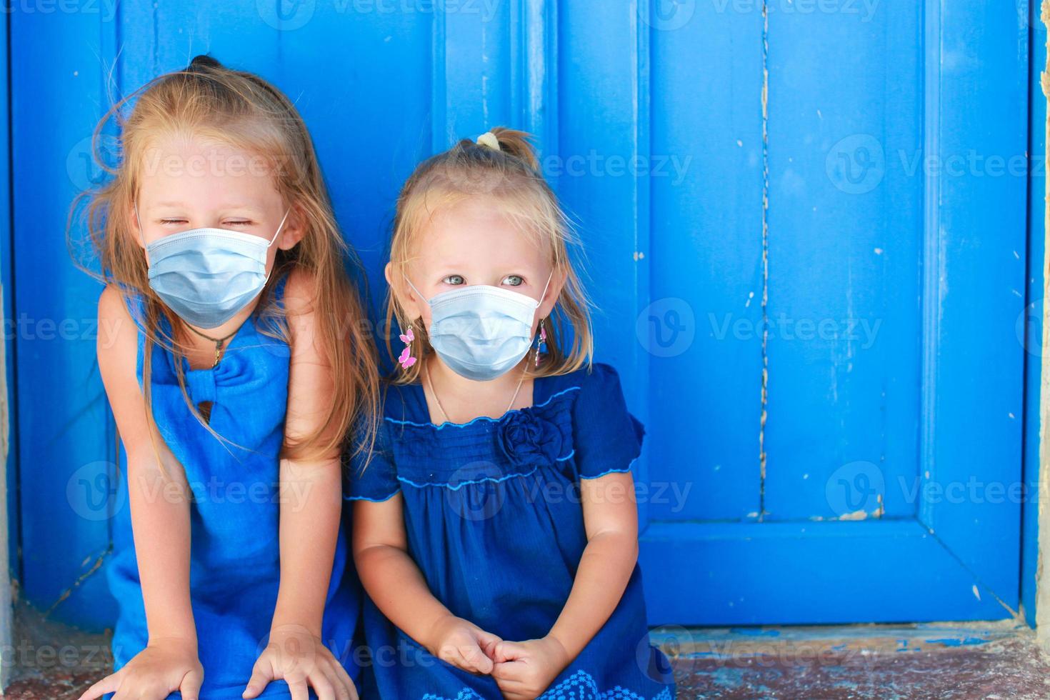 Closeup of Little adorable girls sitting near old blue door in Greek village, Emporio, Santorini photo