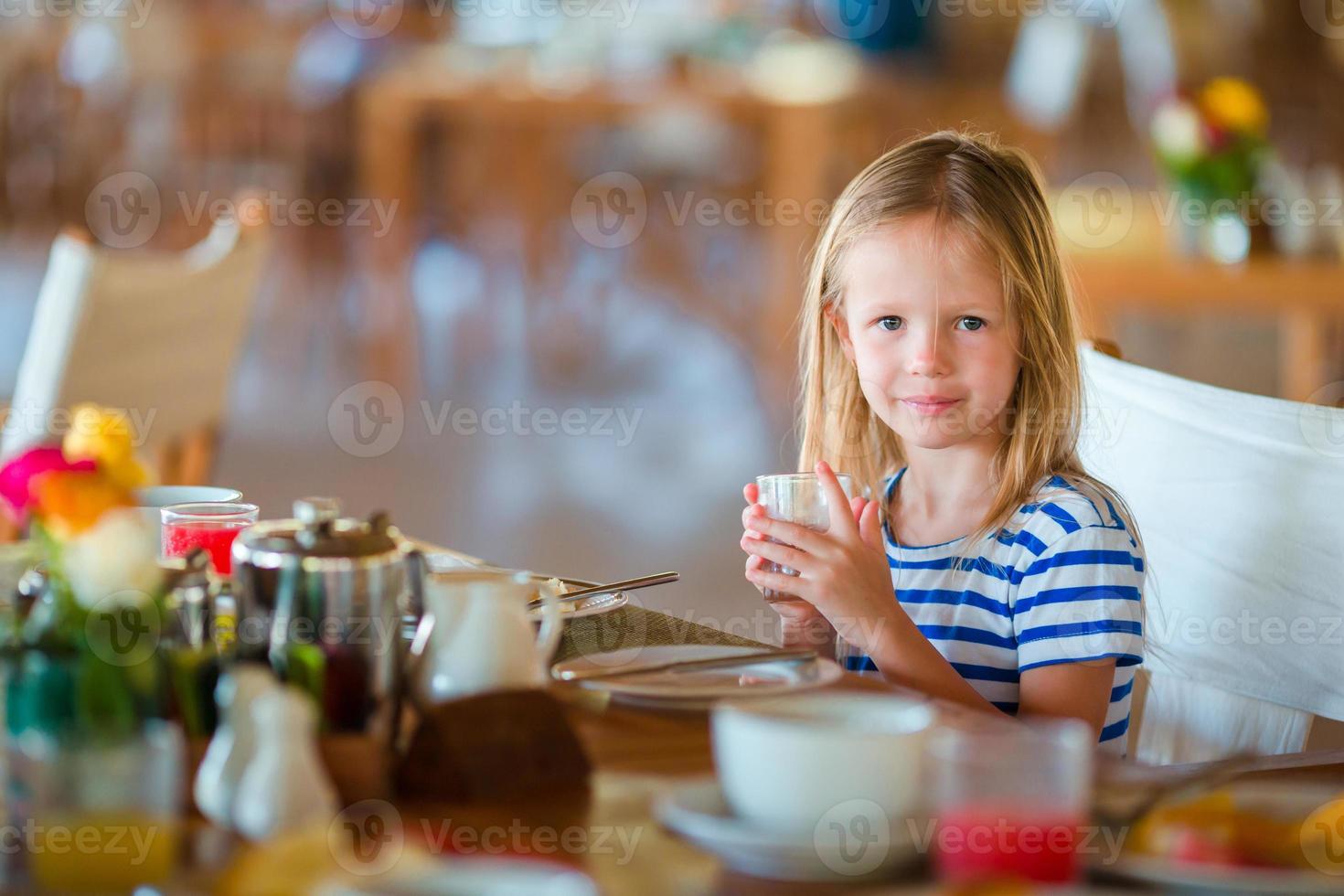 Adorable little girl having breakfast at outdoor cafe photo
