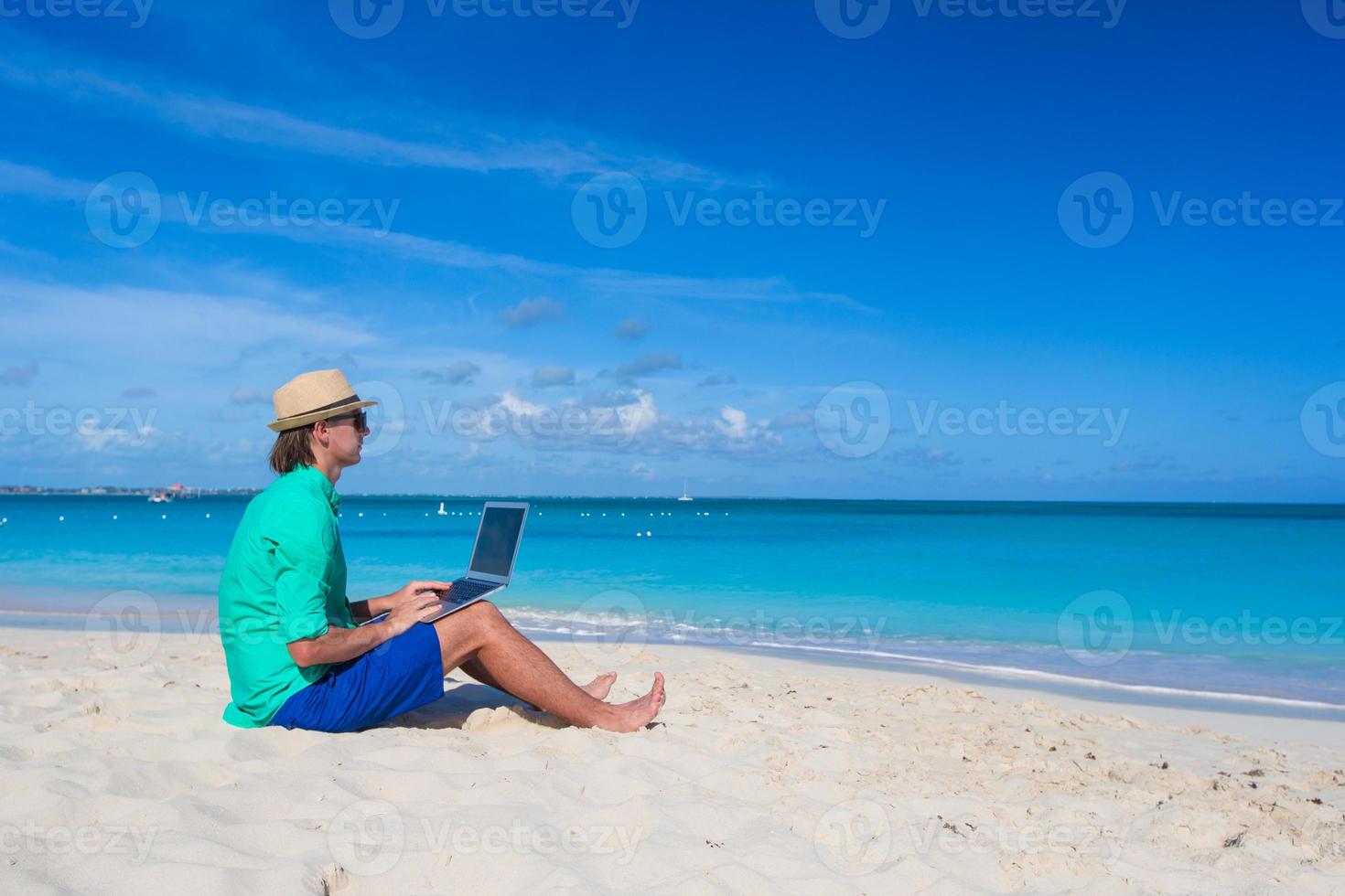 Young man working on laptop at tropical beach photo