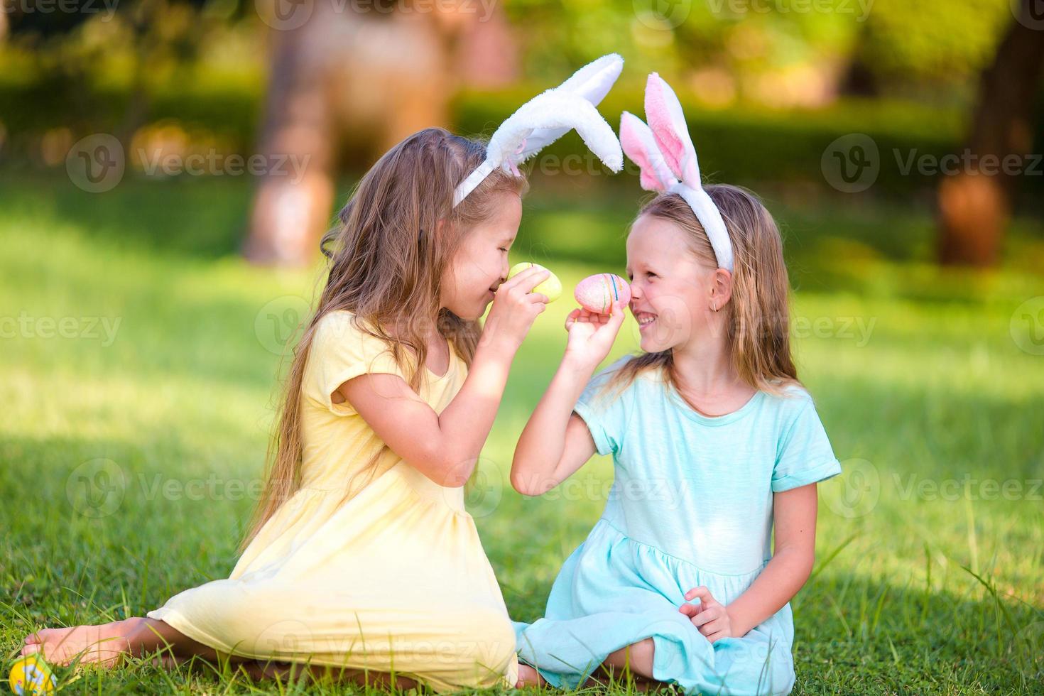 Two adorable little sisters playing with eggs wearing bunny ears on Easter day photo