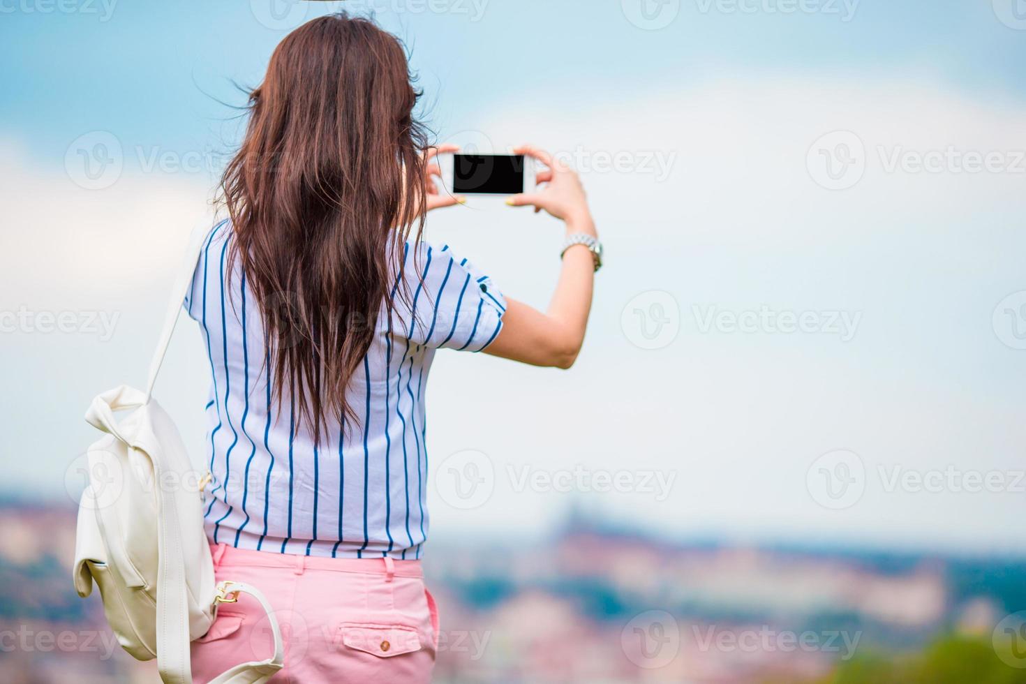 Young caucasian woman making photo of european old city by mobile phone from the observation place