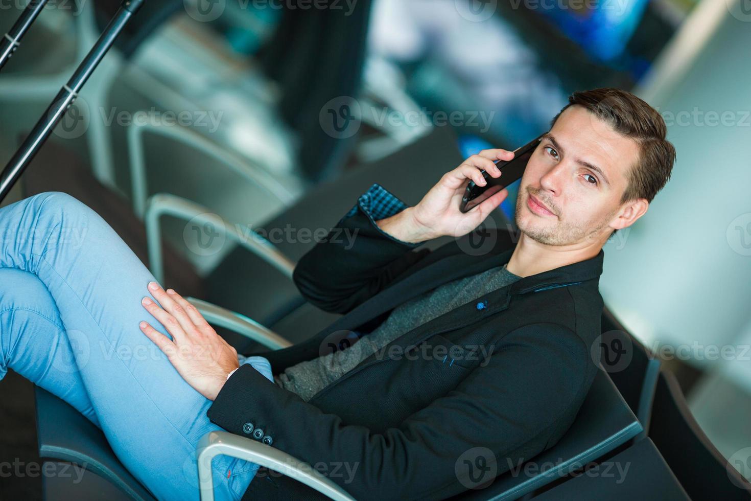 hombre de negocios urbano hablando por teléfono inteligente viajando dentro del aeropuerto. hombre de negocios joven casual con chaqueta de traje. guapo modelo masculino. joven con celular en el aeropuerto mientras espera el embarque. foto