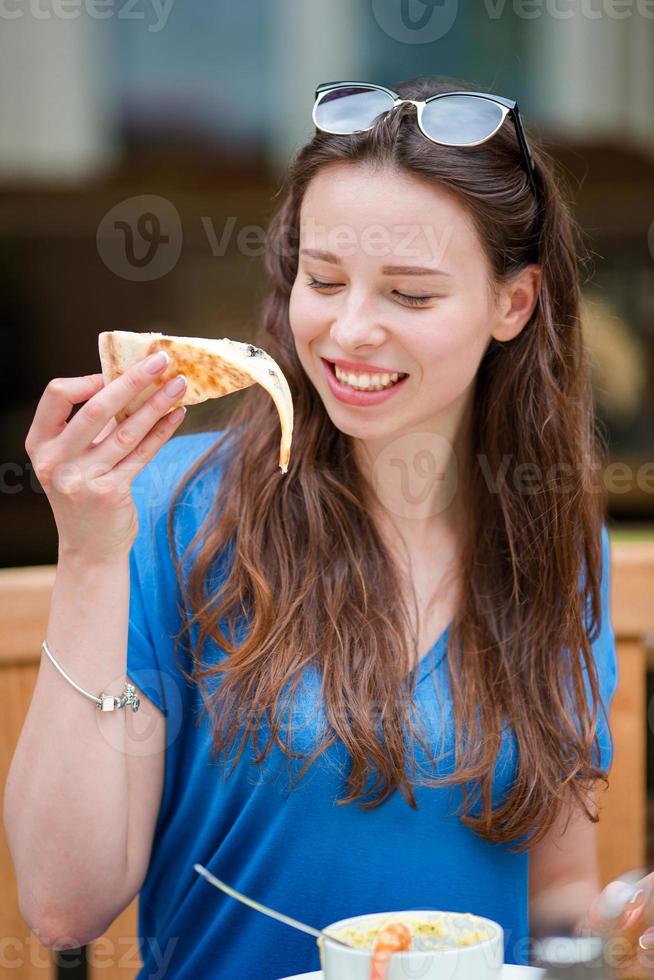 hermosa joven comiendo una rebanada de pizza en un restaurante al aire libre foto