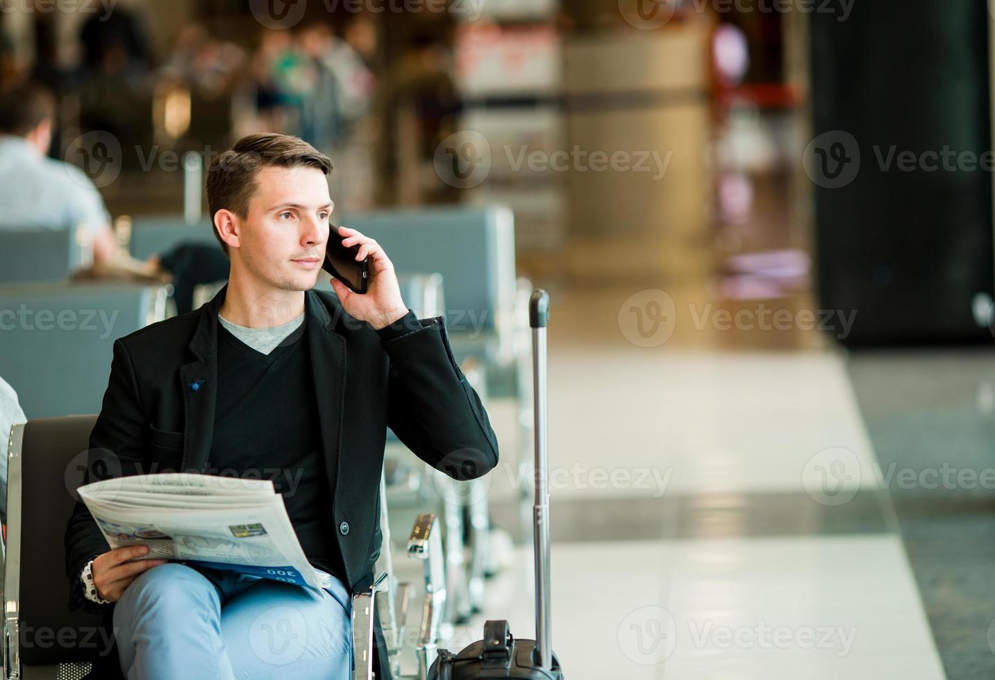 hombre de negocios urbano hablando por teléfono inteligente viajando dentro del aeropuerto. hombre de negocios joven casual con chaqueta de traje. guapo modelo masculino. joven con celular en el aeropuerto mientras espera el embarque. foto
