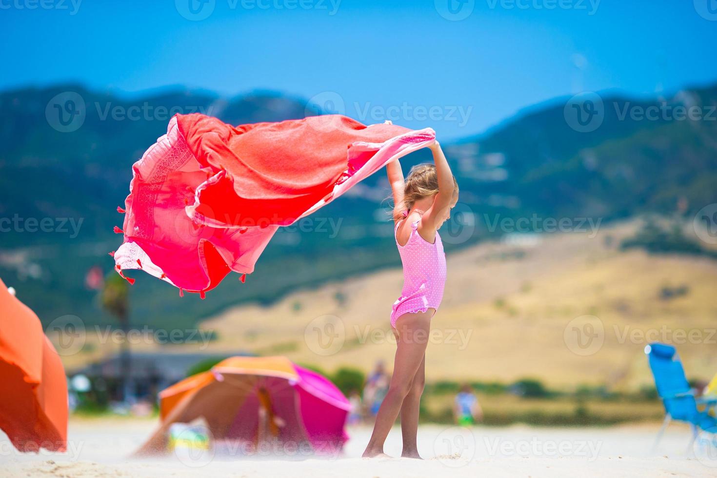 Cute little girl having fun running with towel on tropical beach with white sand and turquoise ocean water photo