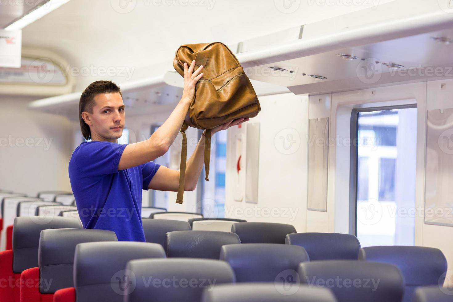 joven poniendo equipaje en el casillero superior en el tren foto