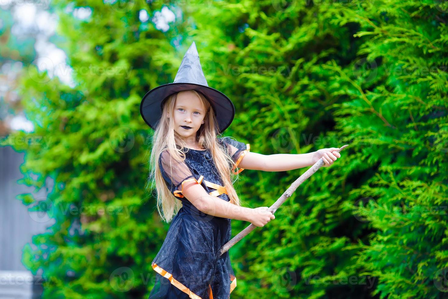 Adorable little girl wearing witch costume with broom on Halloween outdoors photo