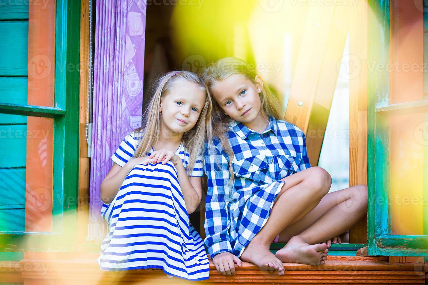 Adorable little girls in the window of rural house outdoors photo
