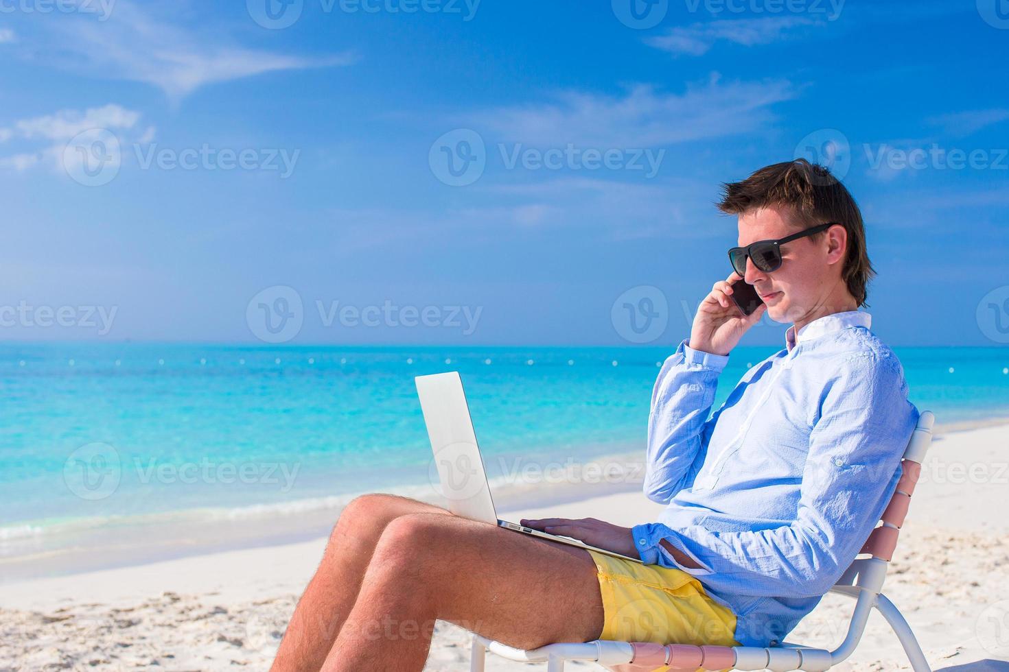 Young businessman using laptop on tropical beach photo