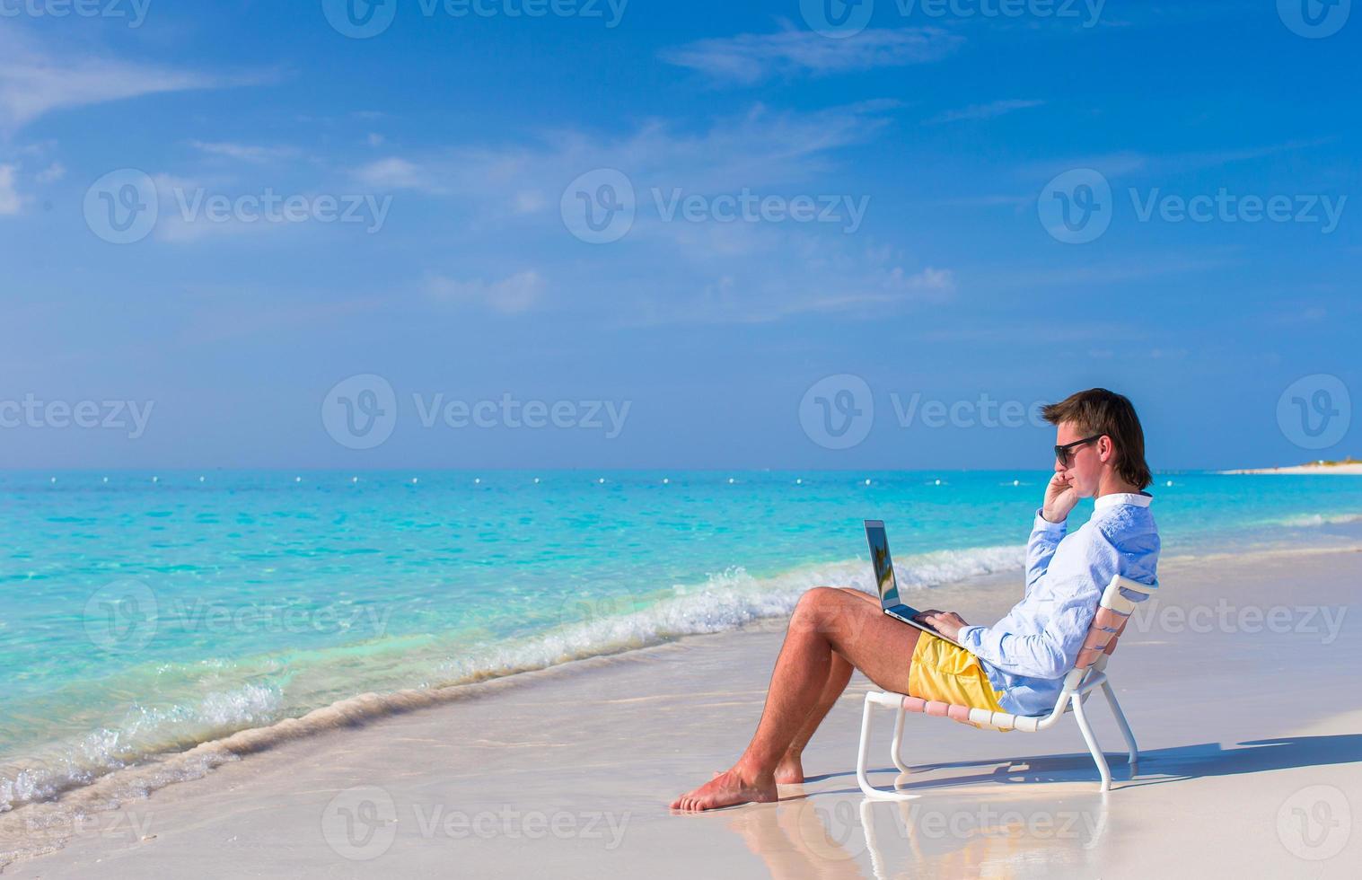 Young man working on laptop at tropical beach photo