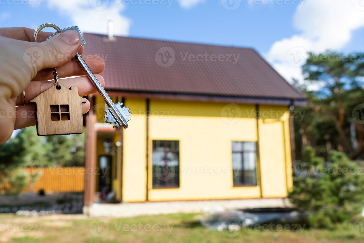 A hand with the keys to a new house on the background of an unfinished cottage. Building, project, moving to a new home, mortgage, rent and purchase real estate. To open the door. Copy space photo