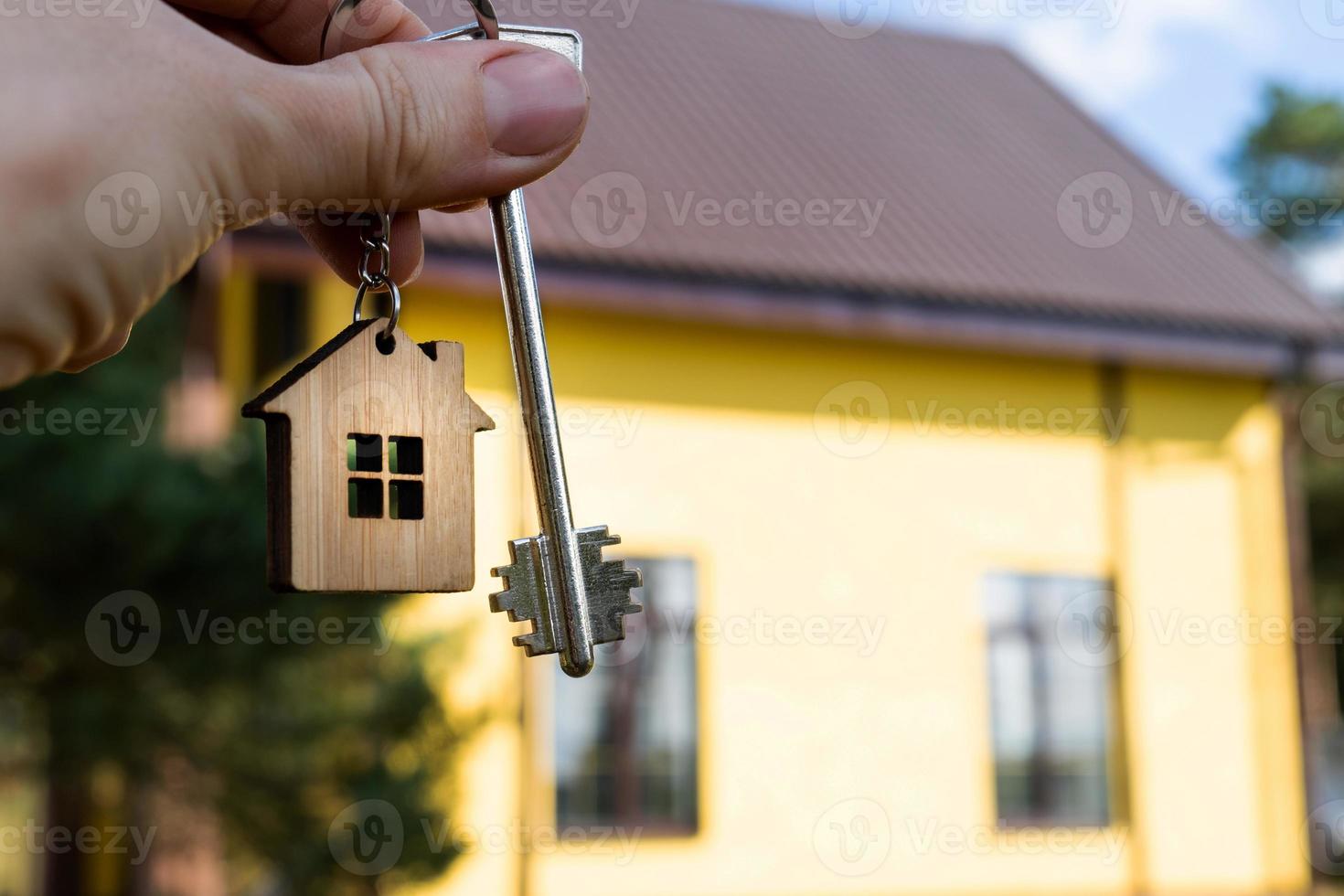 A hand with the keys to a new house on the background of an unfinished cottage. Building, project, moving to a new home, mortgage, rent and purchase real estate. To open the door. Copy space photo