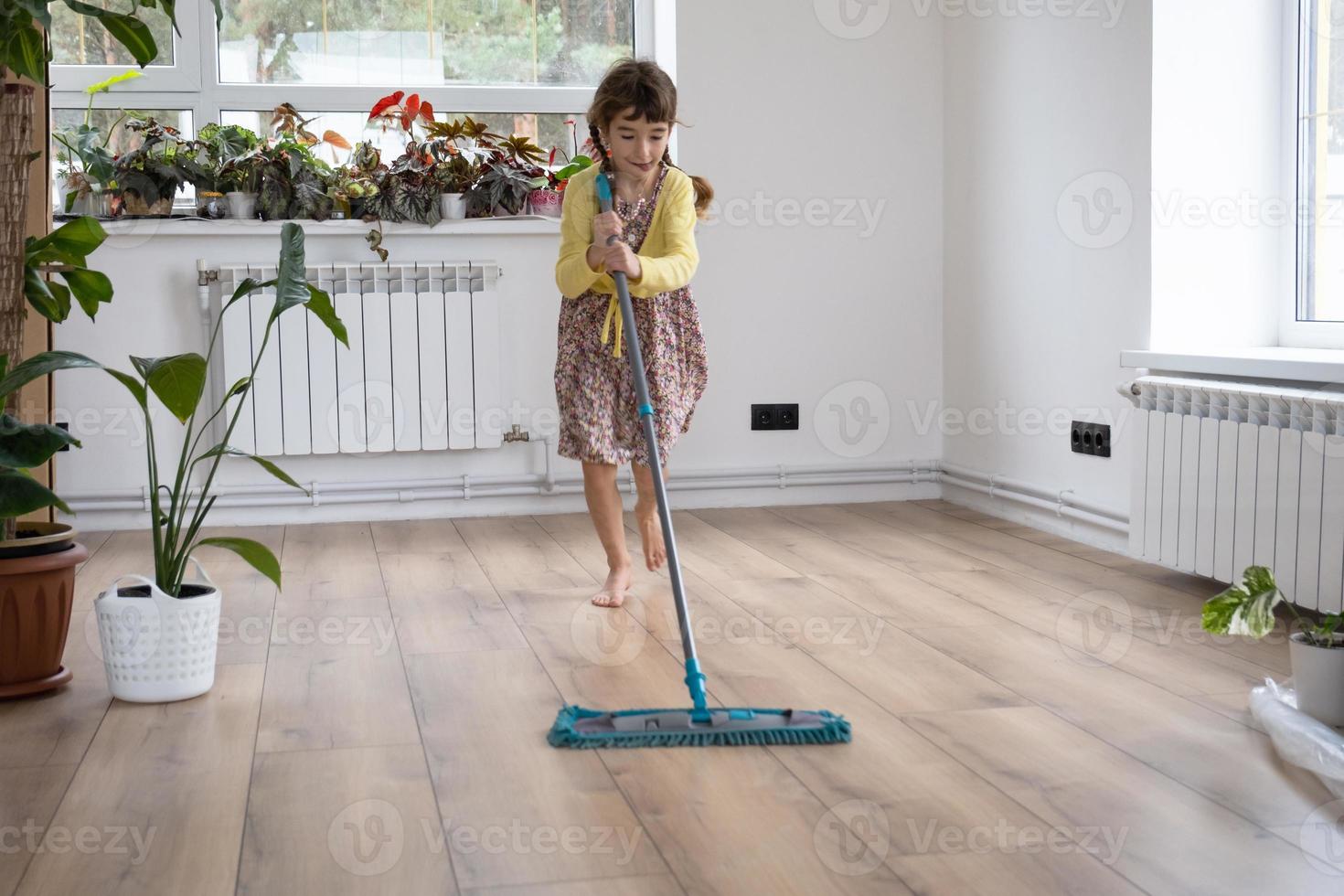 una chica baila con un trapeador para limpiar el suelo en una casa nueva - limpieza general en una habitación vacía, la alegría de moverse, ayuda con las tareas domésticas foto