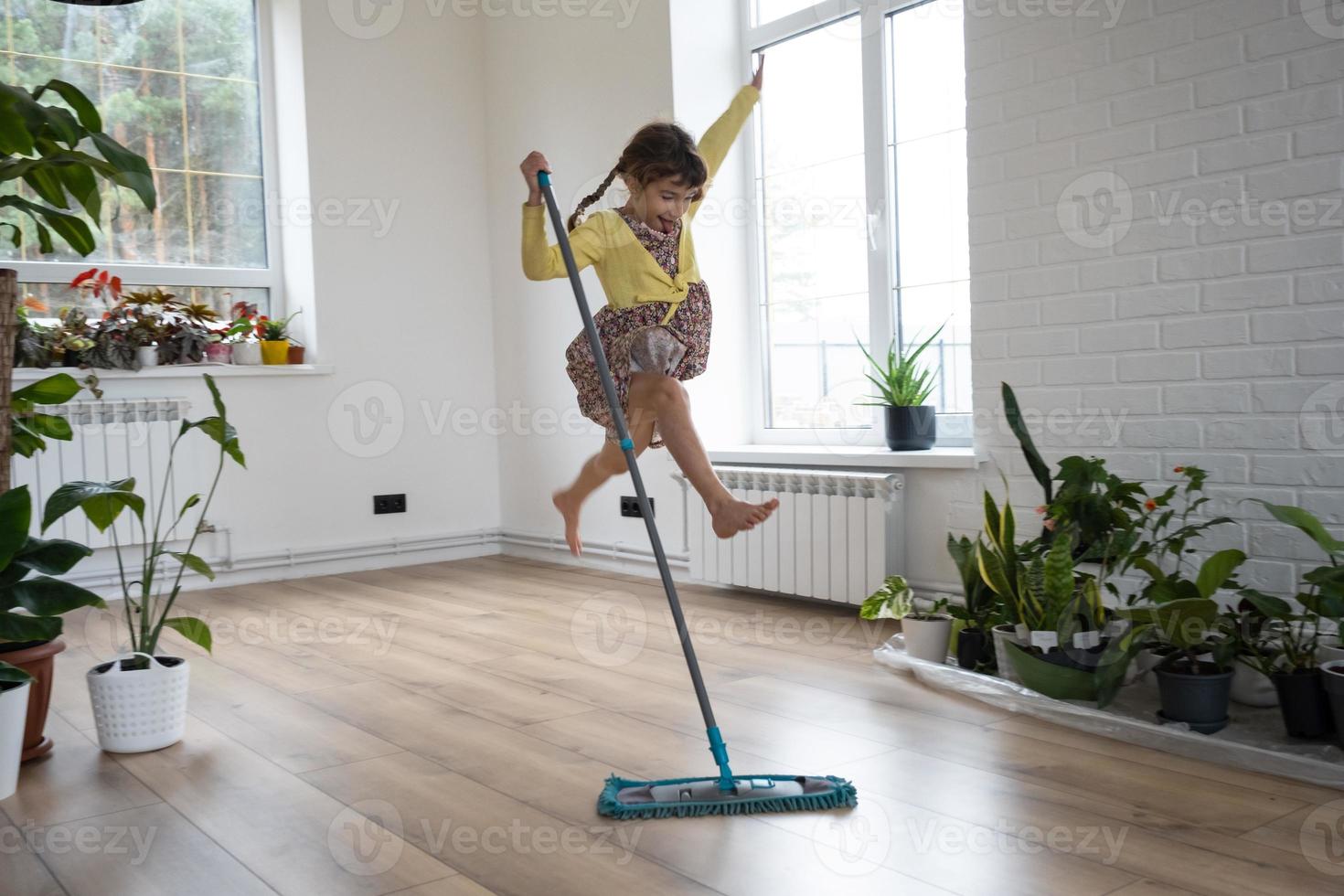 A girl dances with a mop to clean the floor in a new house - general cleaning in an empty room, the joy of moving, help with the housework photo