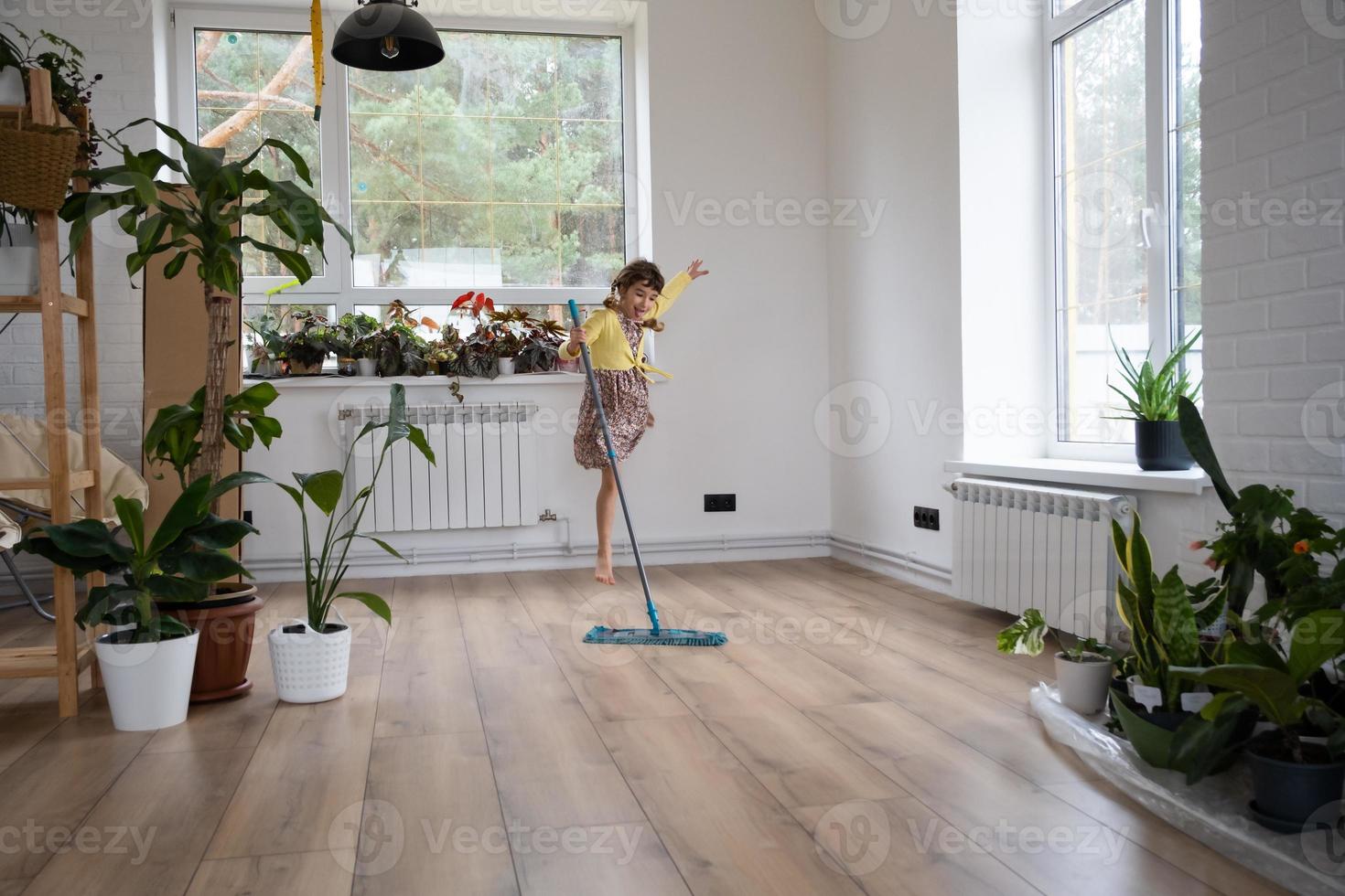 una chica baila con un trapeador para limpiar el suelo en una casa nueva - limpieza general en una habitación vacía, la alegría de moverse, ayuda con las tareas domésticas foto