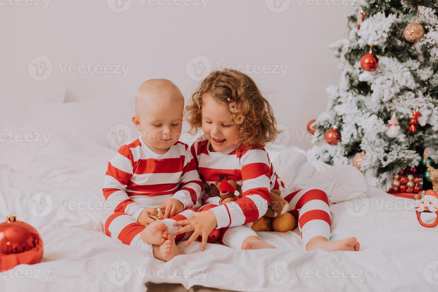 children in red and white pajamas eat Christmas sweets sitting in bed. brother and sister, boy and girl share gifts. christmas morning. lifestyle. space for text. High quality photo