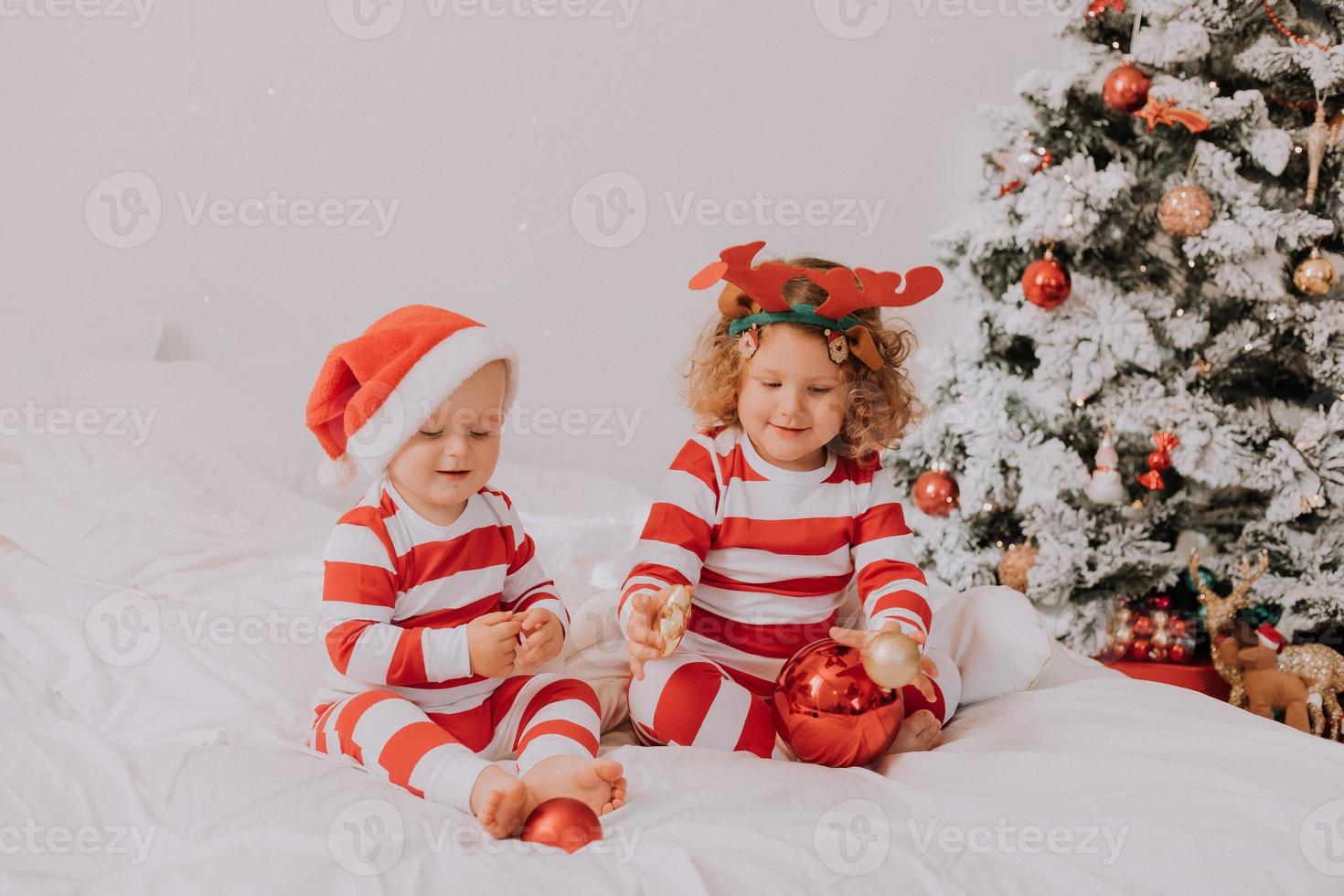 children in red and white pajamas eat Christmas sweets sitting in bed. brother and sister, boy and girl share gifts. christmas morning. lifestyle. space for text. High quality photo