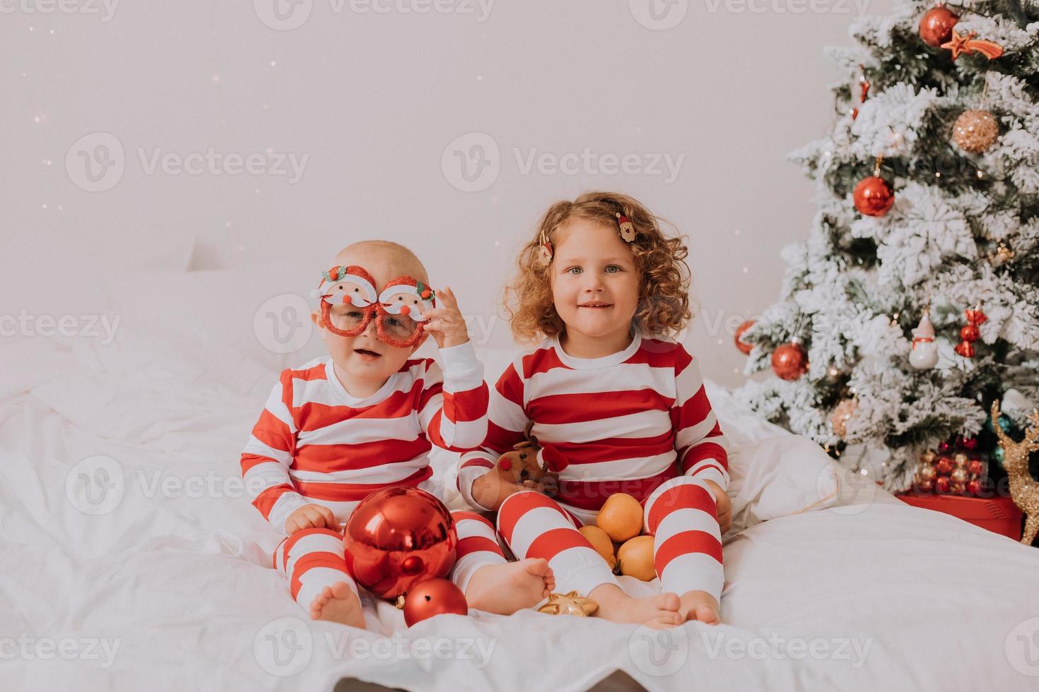 children in red and white pajamas eat Christmas sweets sitting in bed. brother and sister, boy and girl share gifts. christmas morning. lifestyle. space for text. High quality photo