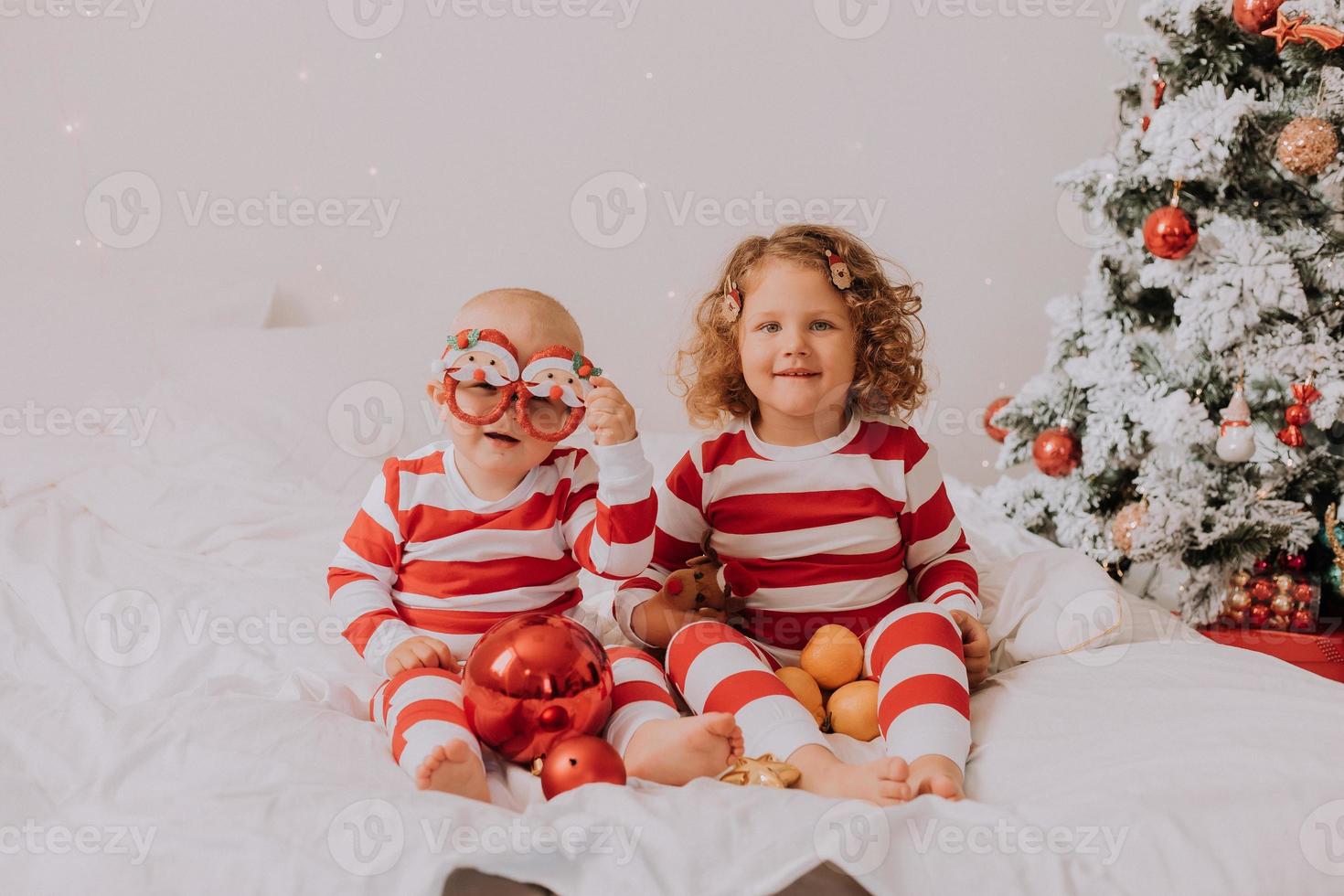 children in red and white pajamas eat Christmas sweets sitting in bed. brother and sister, boy and girl share gifts. christmas morning. lifestyle. space for text. High quality photo