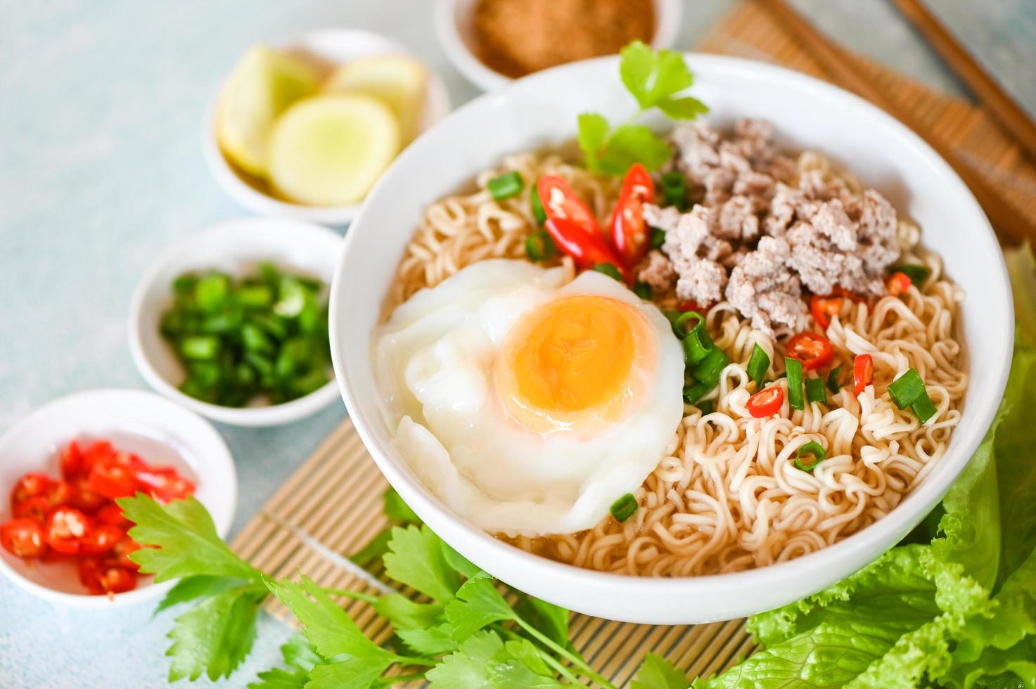 noodles bowl with boiled egg minced pork vegetable spring onion lemon lime lettuce celery and chili on table food , instant noodles cooking tasty eating with bowl - noodle soup photo