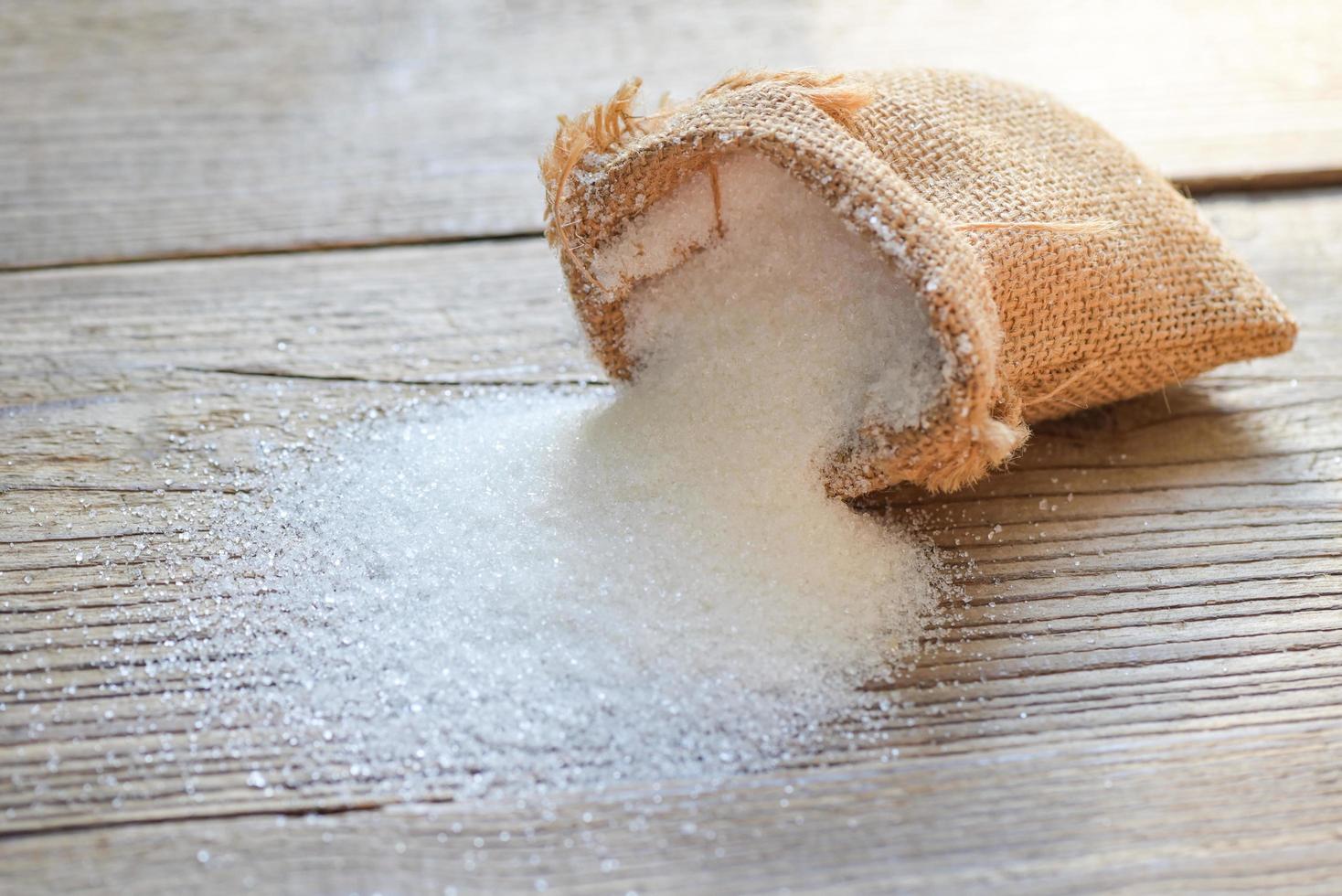 saco de azúcar sobre fondo de madera, azúcar blanco para alimentos y dulces postres dulces montón de azúcar dulce granulado cristalino foto