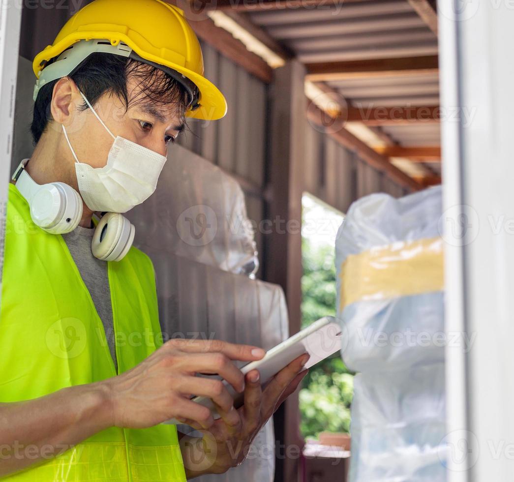 Asian man worker checking the stock of plastic bottles in the warehouse and comparing the balancing number in the system after delivery shipment. Using a tablet to update online stock photo