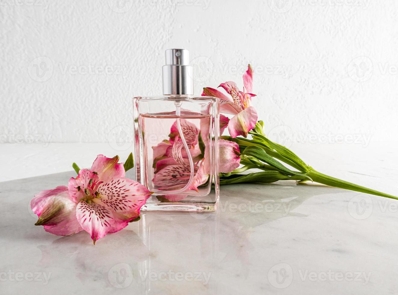 a bottle of perfume on a marble slab against the background of a textured wall and a pink flower. advertising concept of women's parffumeria. photo