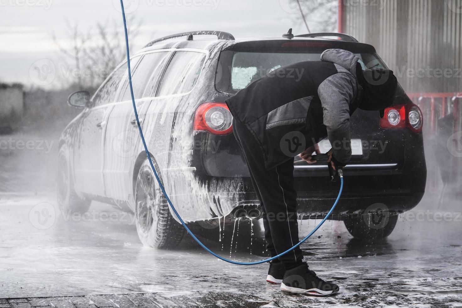 el auto en el lavado de autos está cubierto de espuma, se lava a presión con un chorro de agua foto