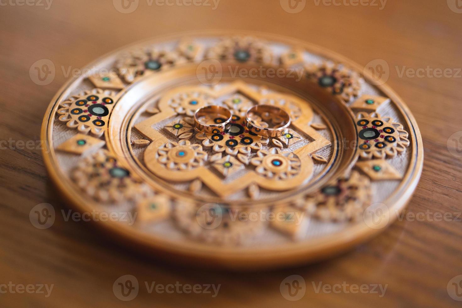 wedding rings on a traditional wooden plate with a pattern photo