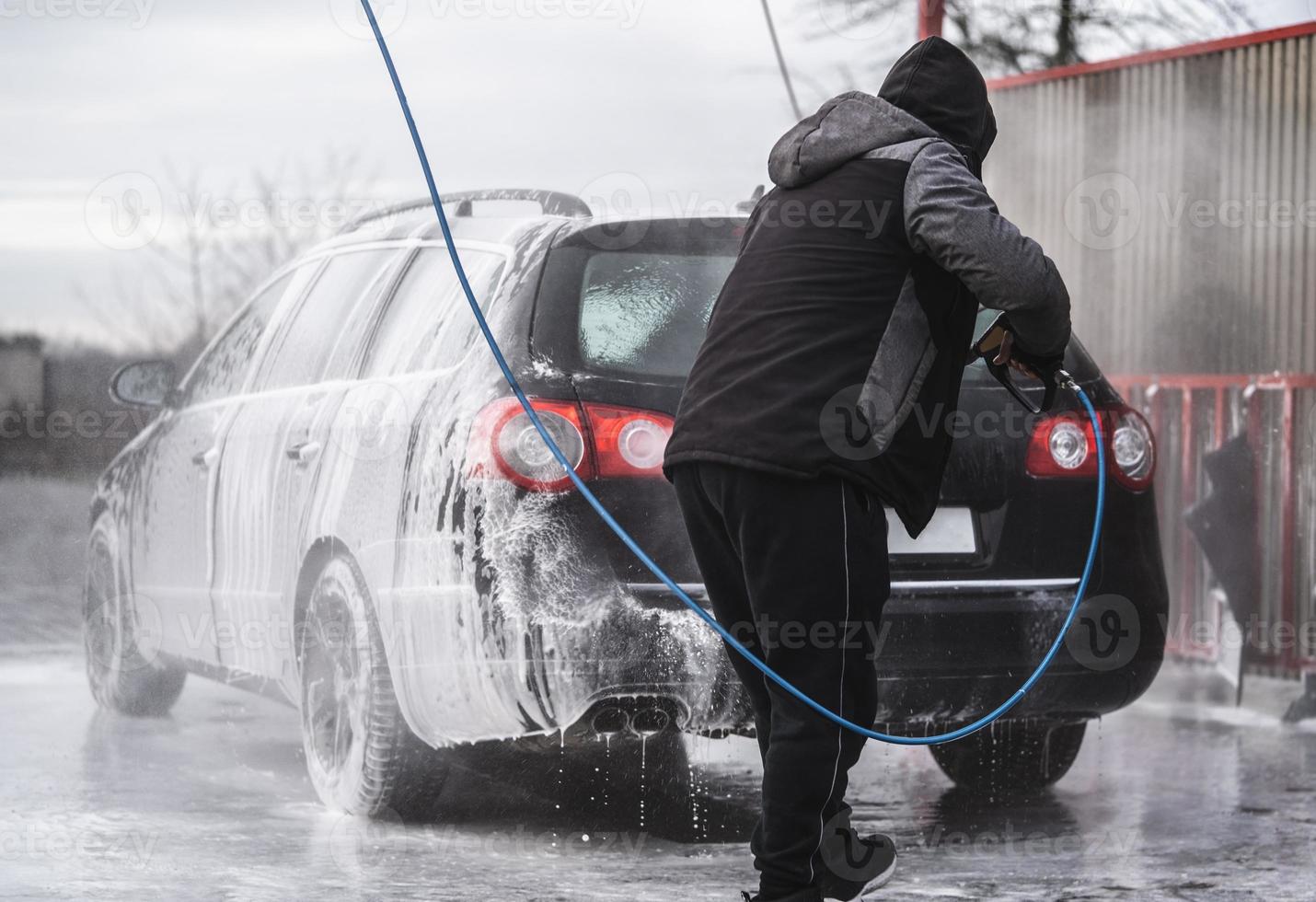 el auto en el lavado de autos está cubierto de espuma, se lava a presión con un chorro de agua foto