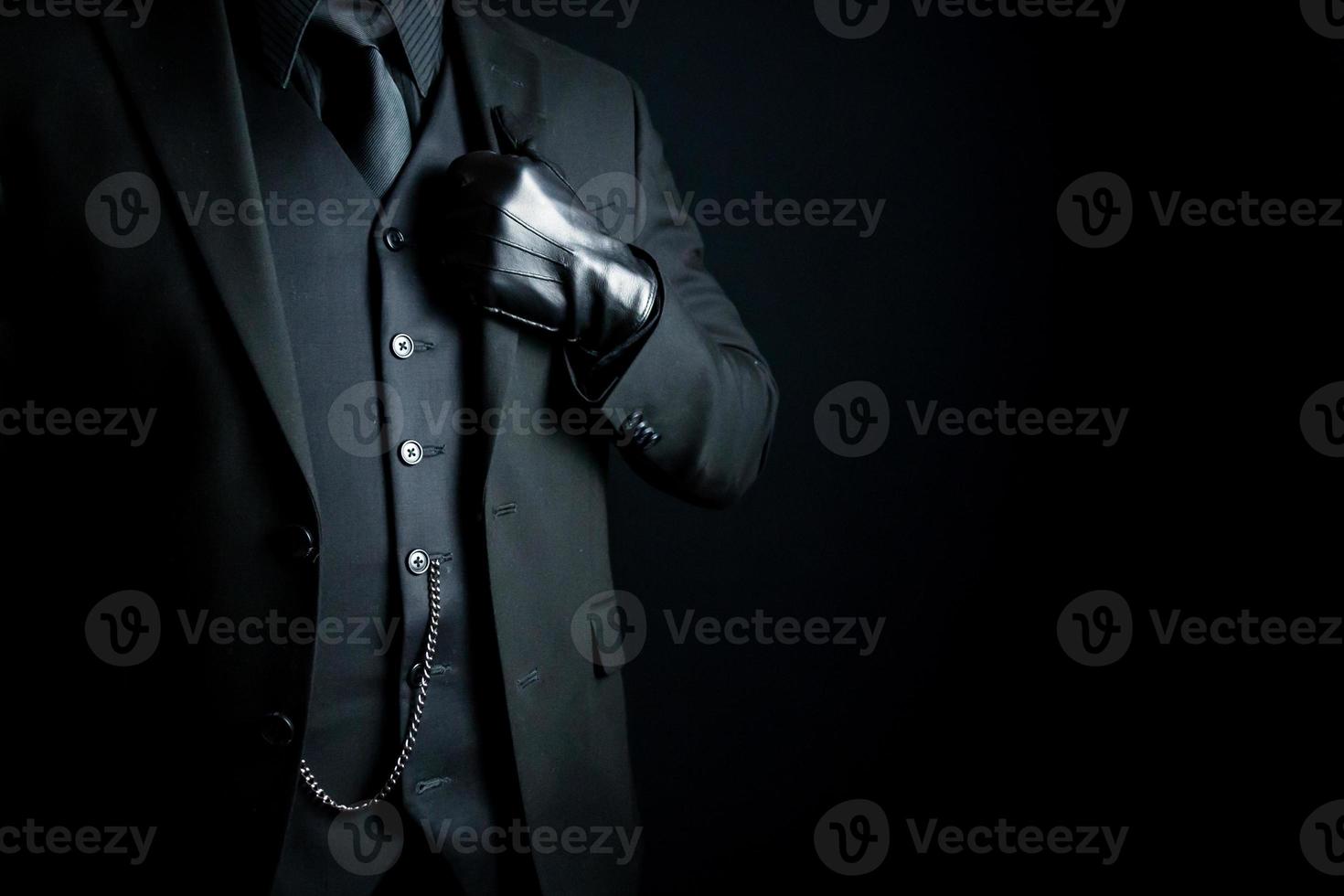 Portrait of Mysterious Man in Dark Suit and Leather Gloves Standing Proudly on Black Background. Concept of Mafia Hitman or Gentleman Assassin. photo