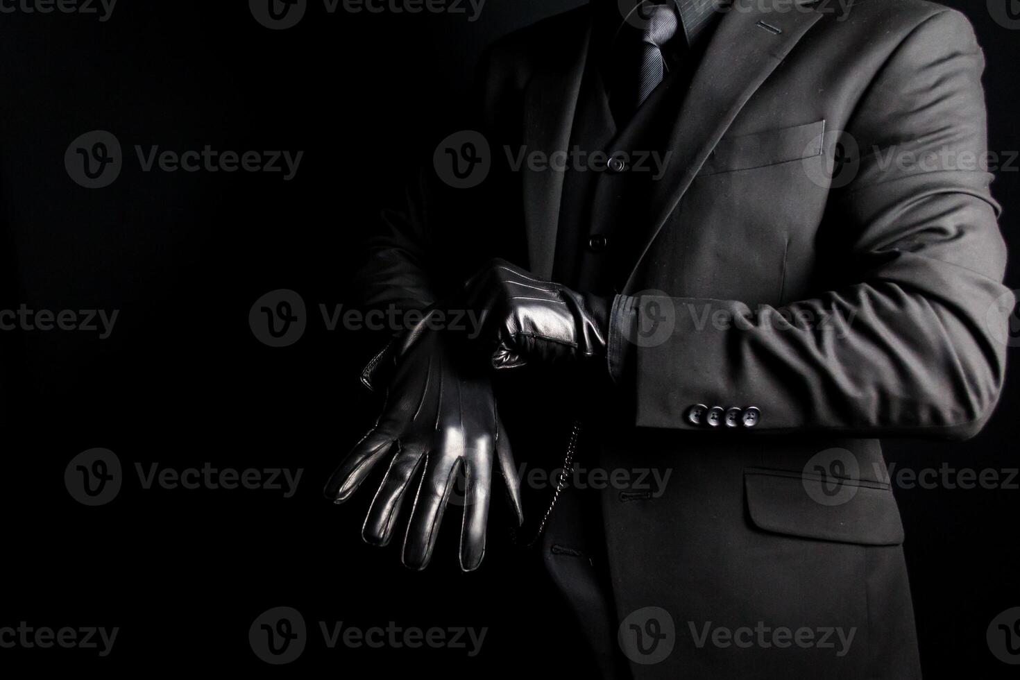 Portrait of Man in Dark Suit Pulling on Leather Gloves on Black Background. Concept of Gangster or Mafia Hit Man. photo