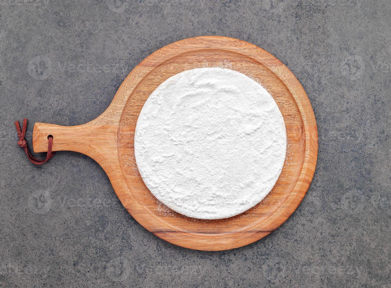 Pizza dough in wooden pizza platter set up on dark concrete. Pizza tray on dark concrete background flat lay and copy space. photo
