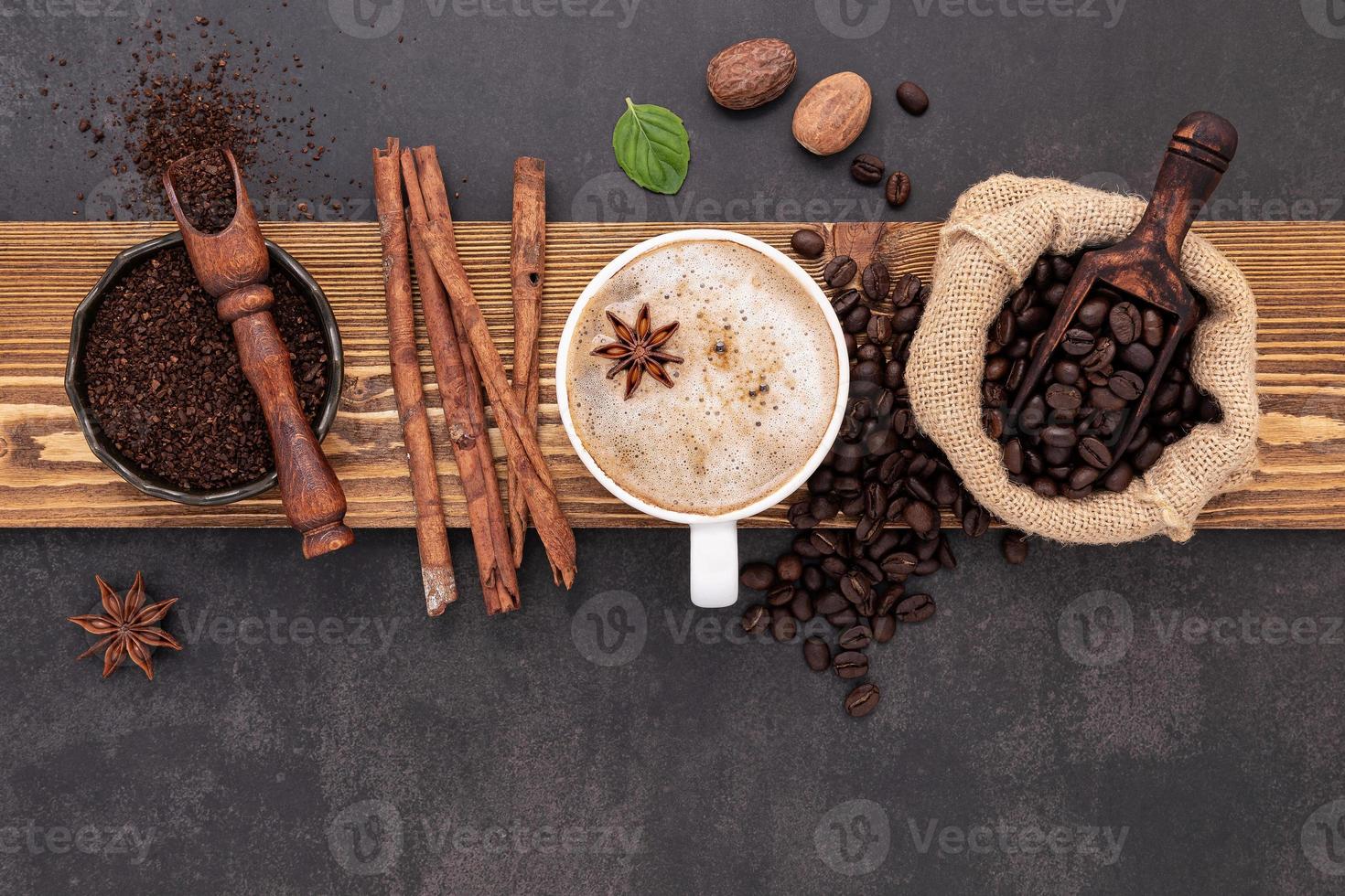 Roasted coffee beans with coffee powder and flavourful ingredients for make tasty coffee setup on dark stone background. photo