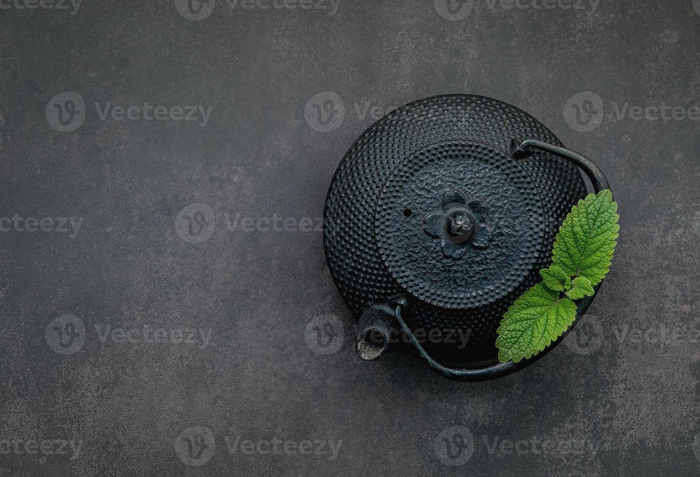 Tetera de hierro fundido negro con té de hierbas sobre fondo de piedra oscura. foto