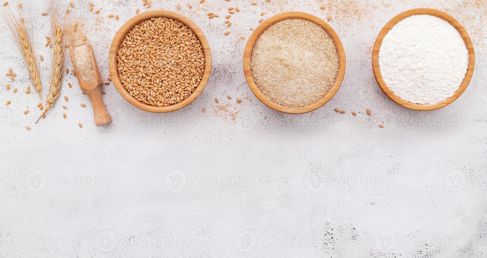Wheat grains , brown wheat flour and white wheat flour in wooden bowl set up on white concrete background. photo