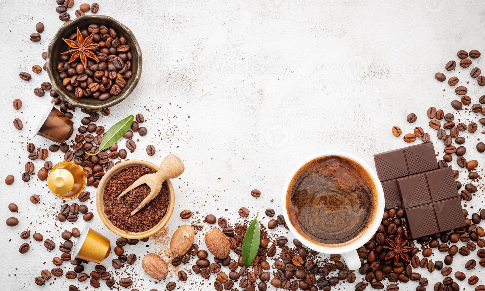 fondo de varios cafés, granos de café tostados oscuros, molido y cápsulas con cucharas colocadas sobre fondo de hormigón blanco con espacio para copiar. foto