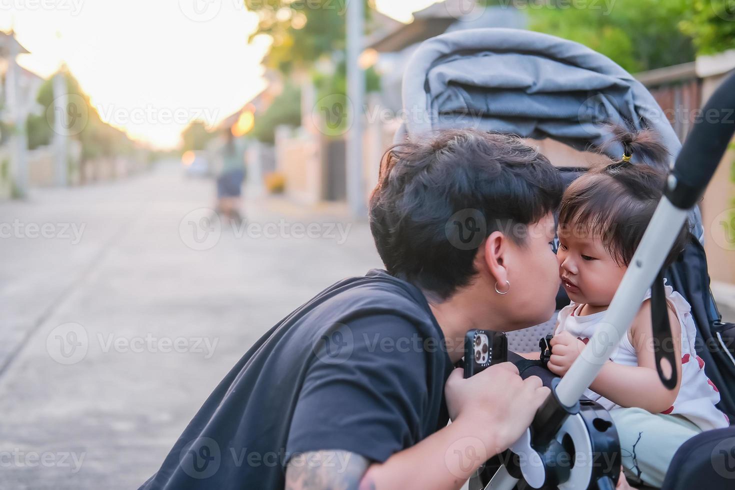 Asian father and daughter or son cute girl making kiss feeling happy and enjoy on baby stroller father and son eye contact smile so showing family love evening with sunlight on face happiness photo