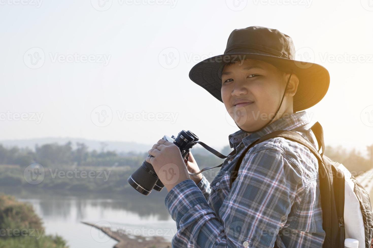 Asian boy is using binoculars to do the birds' watching in tropical forest during summer camp, idea for learning creatures and wildlife animals and insects outside the classroom. photo