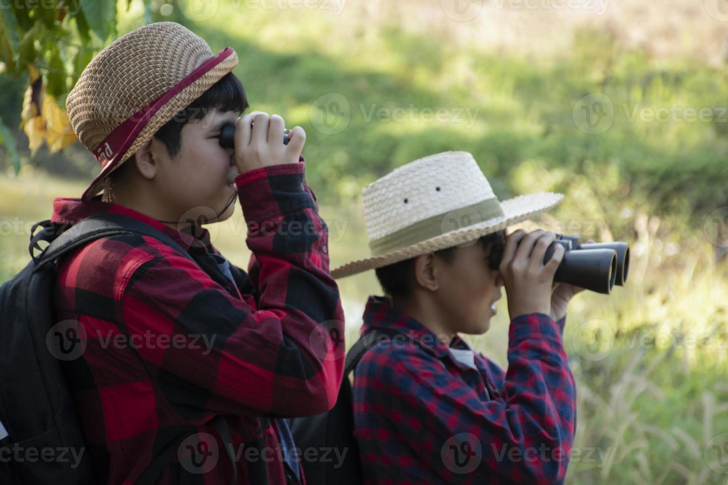Asian boys are using binoculars to do the birds' watching in tropical forest during summer camp, idea for learning creatures and wildlife animals and insects outside the classroom. photo