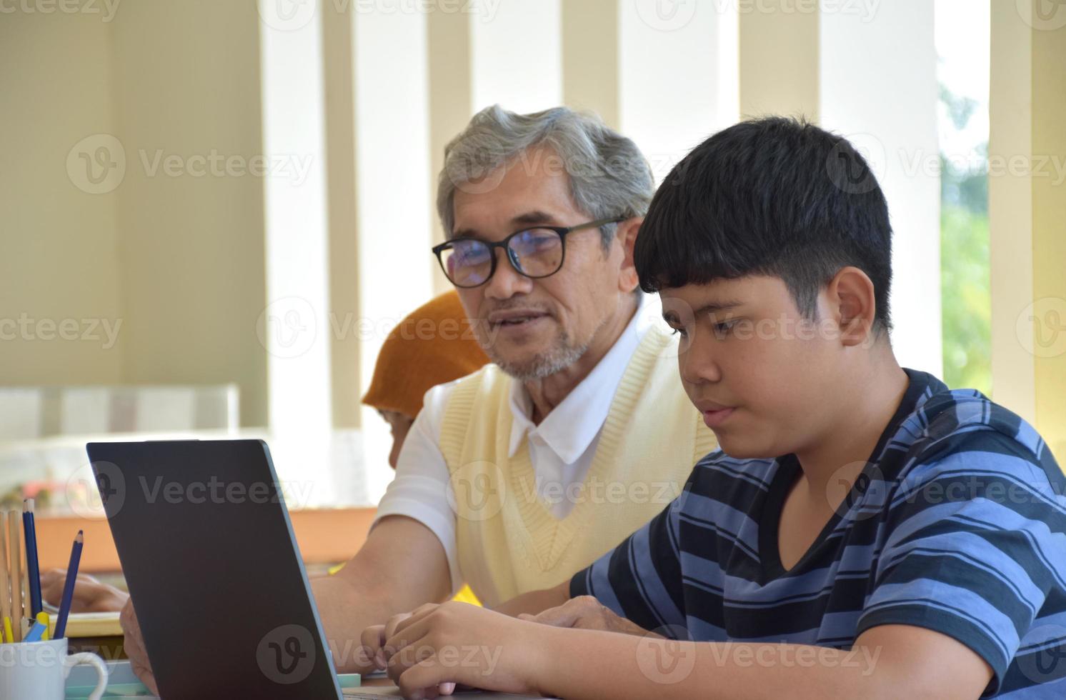 Asian eldery teacher and young teenagers surrounding inside the room to consult and to do the school project work, eldery teacher helps kids to reslove problems and advices them to get a good grade. photo