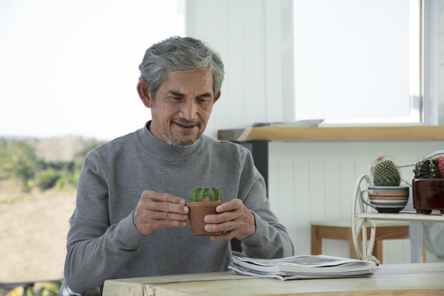 retrata a un anciano asiático sentado cerca de una ventana de vidrio por la mañana para trabajar desde casa y revisando su negocio en su computadora portátil en la mesa con seriedad, enfoque suave y selectivo. foto