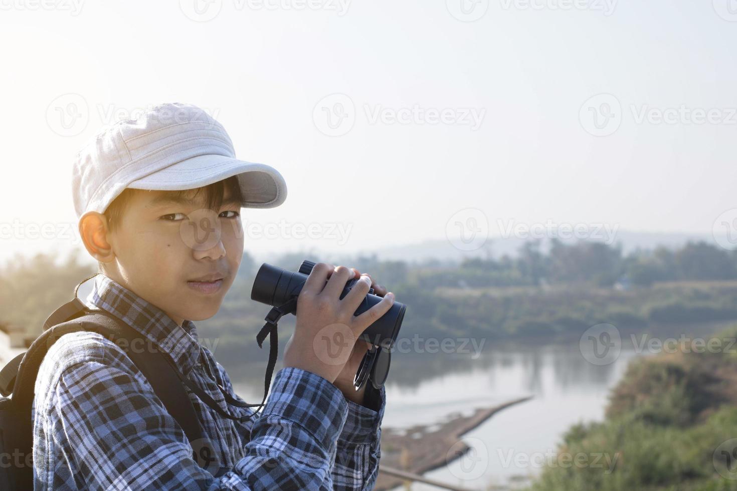 Asian boy is using binoculars to do the birds' watching in tropical forest during summer camp, idea for learning creatures and wildlife animals and insects outside the classroom. photo