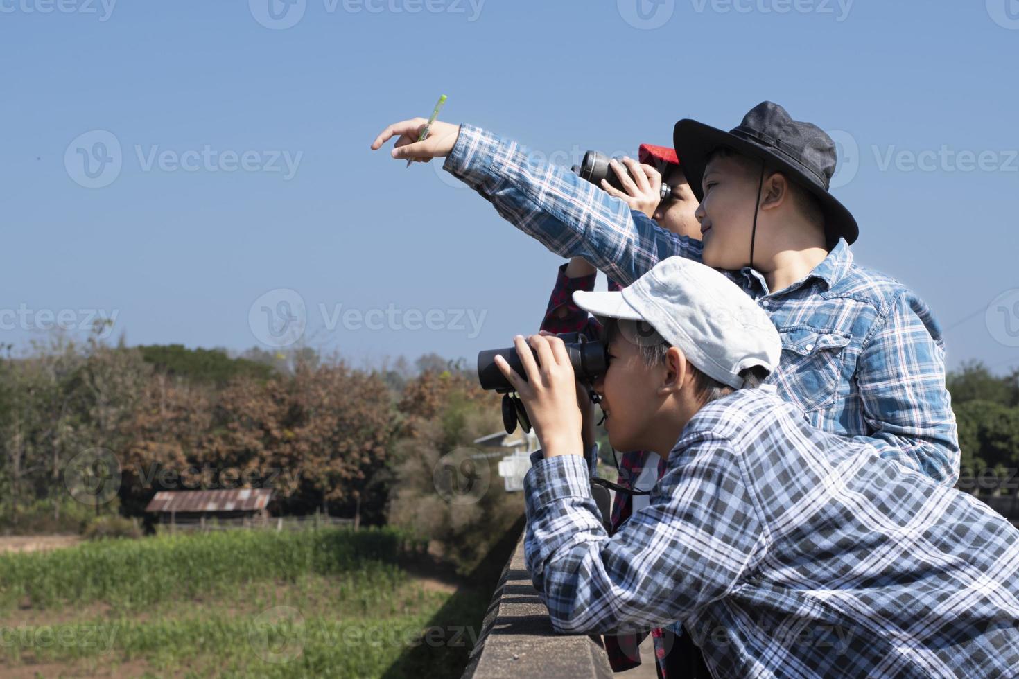 Asian boys are using binoculars to do the birds' watching in tropical forest during summer camp, idea for learning creatures and wildlife animals and insects outside the classroom. photo