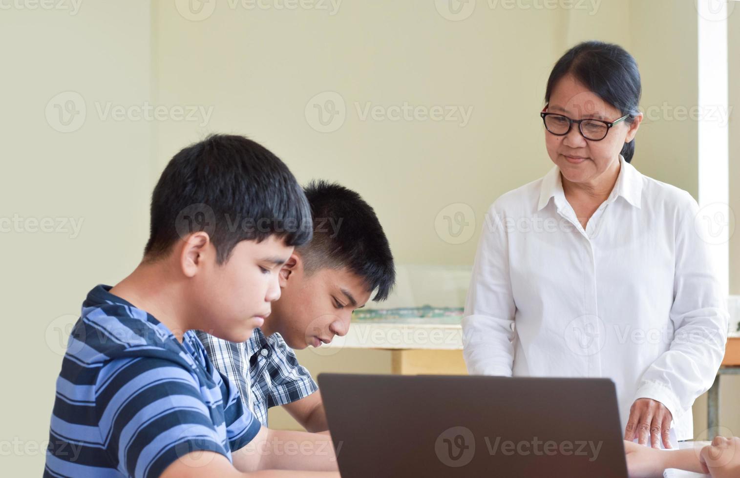 jóvenes adolescentes y maestros asiáticos, están en clase, los estudiantes hacen hojas de trabajo y escuchan sus consejos sobre el proyecto escolar, los adultos ayudan a los niños a hacer el concepto del proyecto escolar. foto