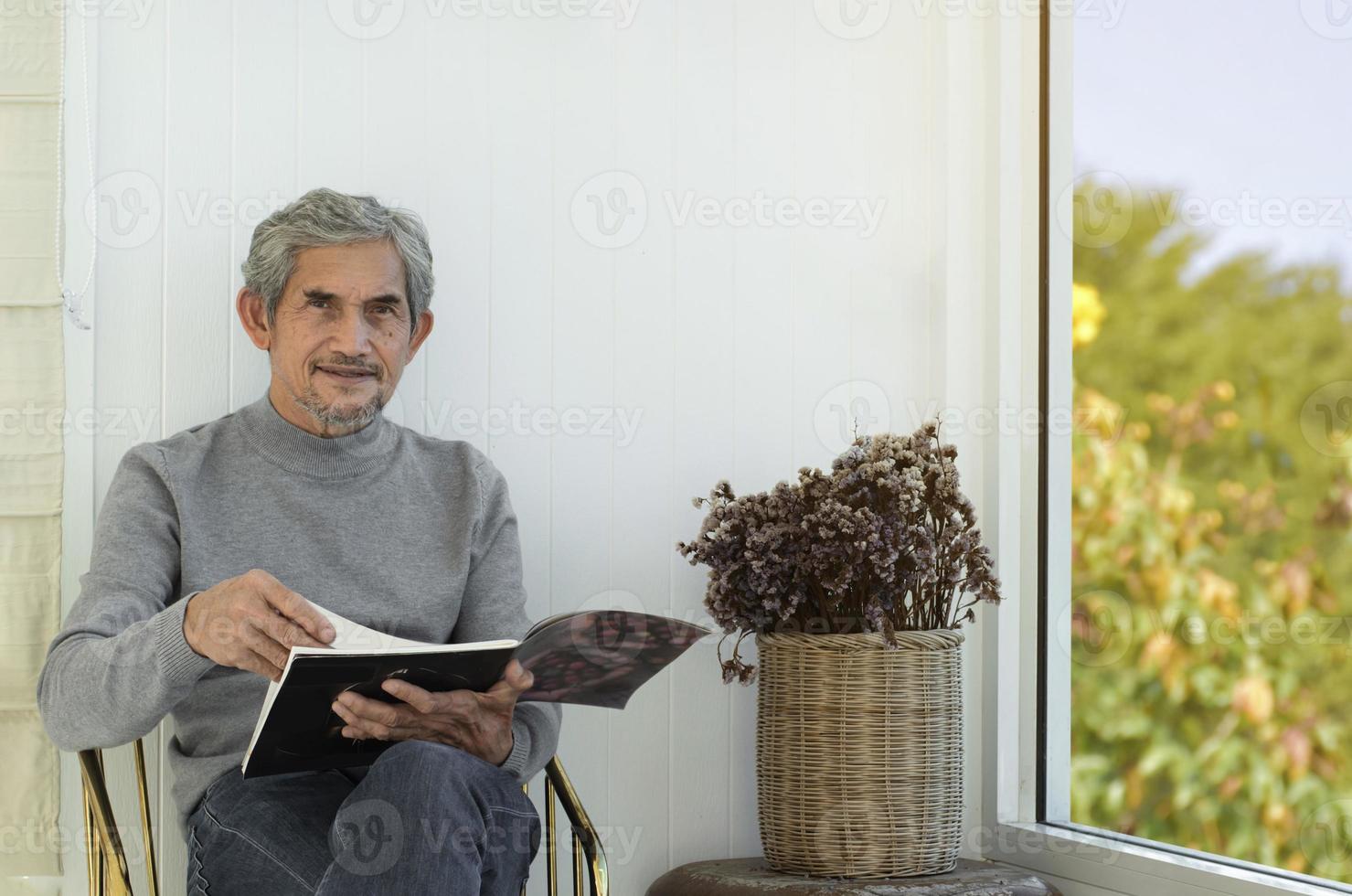 Portrait elderly senior asian man sits near glass window in the morning to work from home and checking his business on his laptop on table seriously, soft and selective focus. photo