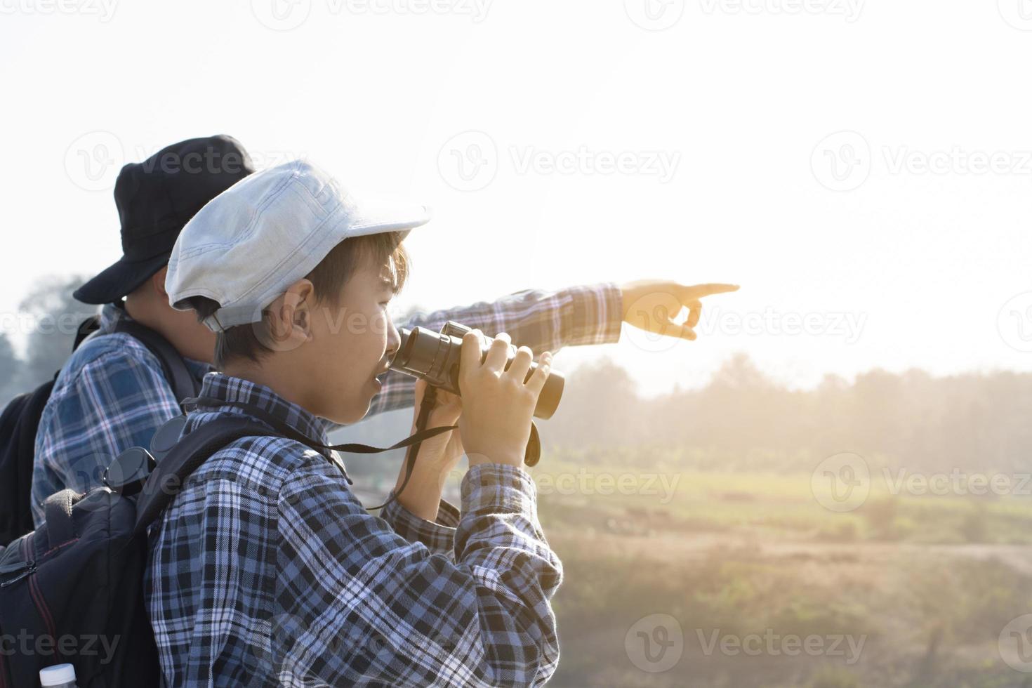 Asian boys are using binoculars to do the birds' watching in tropical forest during summer camp, idea for learning creatures and wildlife animals and insects outside the classroom. photo